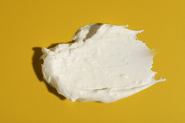 Cream on dark yellow background, top view. Sample of cosmetic product