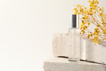 Bottle of serum and yellow gypsophila flowers on concrete blocks against white background, space...