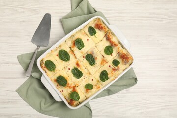 Delicious spinach lasagne in baking dish served on white wooden table, flat lay