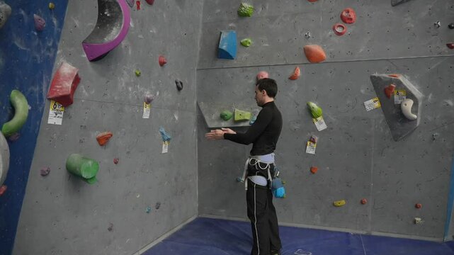 Caucasian man uses talc on a climbing wall. 