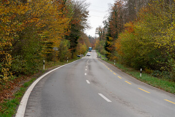 Road in the late afternoon. A car and a truck are driving on the road through the autumn forest.