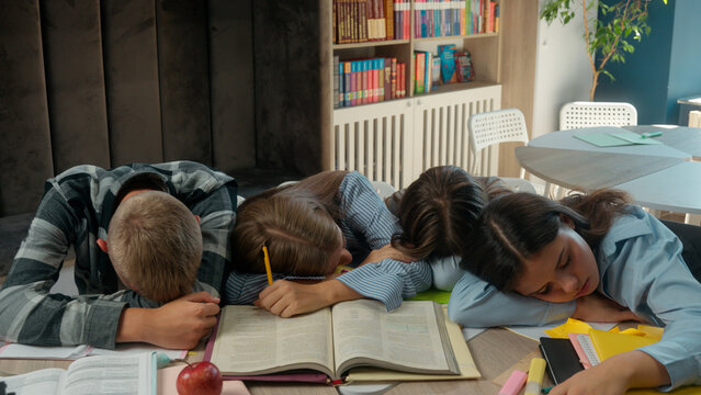 Caucasian four friends pupils tired exhausted fatigued students teens and teenagers boy guy male girls female at school library class sleeping napping on table books sleep together studying education