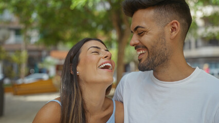 Obraz premium Man and woman laughing together in an urban park, showcasing a joyful relationship and beautiful connection outdoors.
