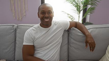 Young man sitting on a couch in a cozy living room, smiling warmly and exuding confidence in a...