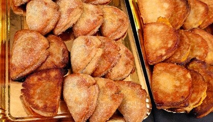 Golden trays with crispy, half-moon-shaped pastries; left tray has sugar-dusted ones with a rough texture, right tray has smoother pastries with a darker crust;