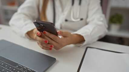Woman using mobile phone at workplace in clinic setting with stethoscope visible, depicting a professional healthcare environment focusing on communication technology.