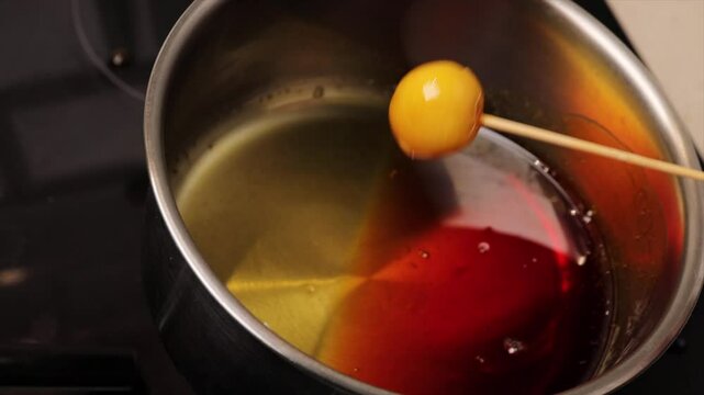 Dipping coconut balls of Brazilian dessert bala baiana in sugar syrup. Traditional caramelized coconut treat preparation.