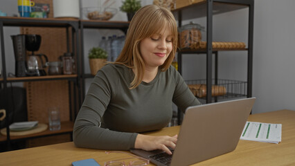 Woman working on laptop in modern office surrounded by shelves and coffee maker, showcasing a relaxed and productive work environment during the day.