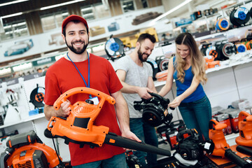 Salesman is posing with new leaf blower with couple of clients in background in power tools store.