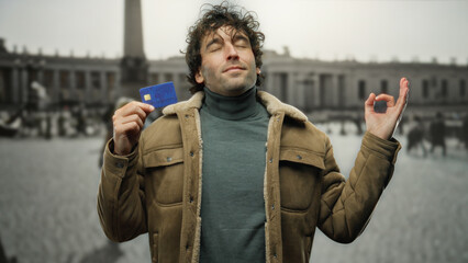 Young hispanic man holding credit card in front of saint peter's square in vatican city, embracing...
