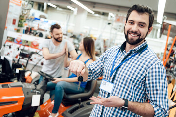 Obraz premium Salesman is posing with couple of clients and keys for cleaning machine in power tools store.