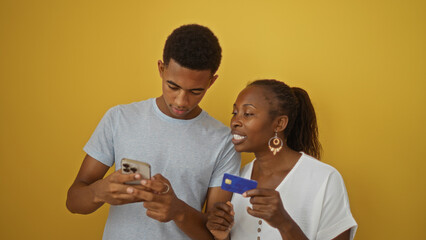 Mother and son using smartphone and credit card on yellow background demonstrating modern family interaction