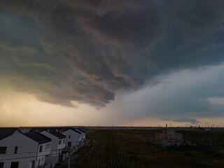 Fototapeta premium Rural settlement on the plain filmed from drone in cloudy summer weather. Beginning of a strong storm accompanied by thunder and lightning
