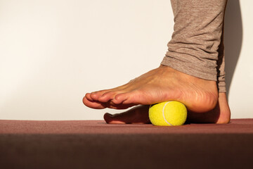 Myofascial relaxation of the muscles of the foot with a tennis ball on a mat at home, close-up. Concept on the topic of preventing foot pain