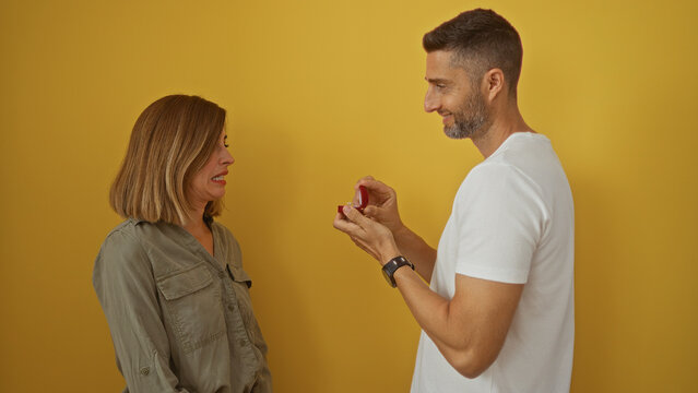 Woman showing disgust as man proposes with ring over isolated yellow background - Powered by Adobe