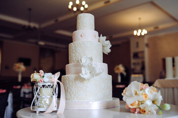 Wedding cake with floral lace design, white flowers, and soft pink accents, with a bouquet nearby.
