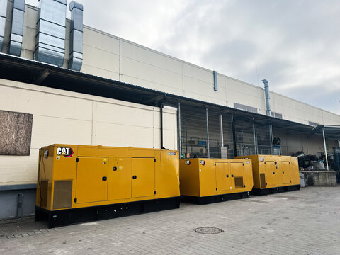 Lviv, Ukraine - February 12, 2025: Industrial yellow CAT generators outside a modern facility under overcast sky