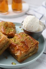 Delicious baklava with crushed nuts and ice cream on white wooden table, closeup