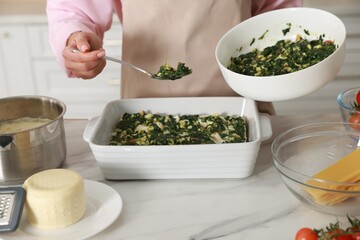 Woman making spinach lasagna at marble table indoors, closeup