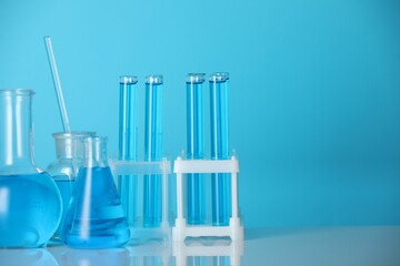 Laboratory glassware with liquid on mirror surface against blue background. Space for text
