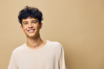 smiling young man with curly hair wearing a light colored shirt against a neutral beige background, exuding joy and confidence, ideal for lifestyle or portrait photography
