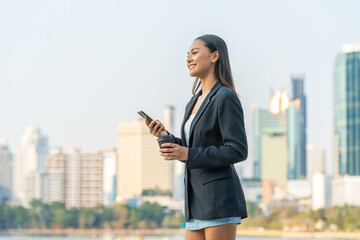 Young Asian Businesswoman Using Phone While Holding Coffee in Modern City Outdoors © StockPhotoRepublic
