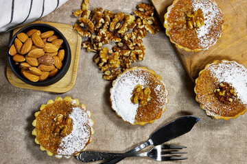 Delicious homemade chocolate  tarts named Amandines in frensh surrounded by walnuts and almonds being presented on a table