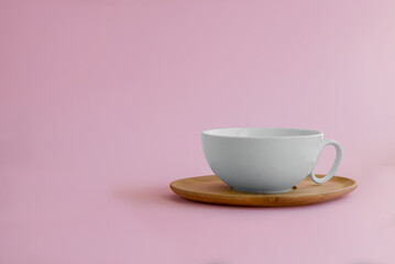 On a pink background, a white cup on a wooden saucer. The concept of tableware for tea and coffee.
