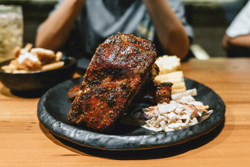 A plate of ribs and corn on a table with a person looking at it. Scene is that of someone enjoying a delicious meal. for all business