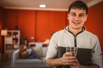 Portrait of handsome young man stand and hold glass of water at home