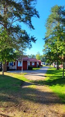 Bright red cottages are surrounded by lush greenery in a camping site. Visitors enjoy the sun and relax outside as summer vibes fill the atmosphere. A peaceful retreat in nature.