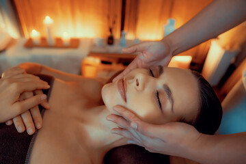 Caucasian woman enjoying relaxing anti-stress head massage and pampering facial beauty skin recreation leisure in warm candle lighting ambient salon spa in luxury resort or hotel. Quiescent