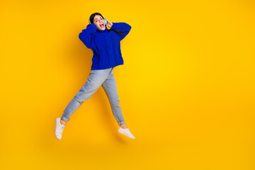 Excited young woman in a blue pullover leaping against a bright yellow backdrop, displaying vibrant energy and joy