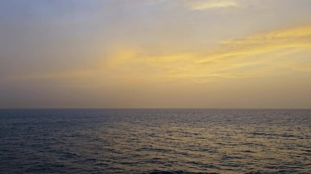 Golden clouds over over the horizon above a tranquil sea-At sea