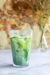 a glass of matcha latte with ice on white marble table.