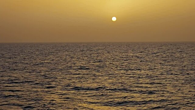 Sun low on the horizon through hazy amber clouds over peaceful ocean - View at sea