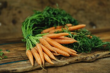 Vibrant orange carrots with lush green tops rest on a rustic wooden surface, showcasing the essence...