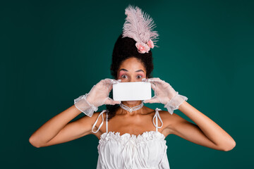 Young woman in baroque costume holding a blank sign against elegant green backdrop, merging...