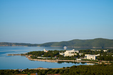 Overlooking a peaceful bay, lush green hills encircle a captivating shoreline dotted with buildings, reflecting the beauty of a sunny afternoon in a coastal paradise.