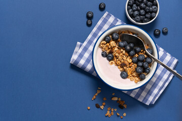 Bowl with blueberry greek yogurt and oat granola on blue background with copy space. Food breakfast...