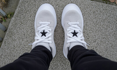 Aerial View of White Sneakers on Gray Surface with Black Star Detail Captured in Urban Setting for Fashion or Lifestyle Concept