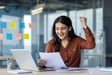 Successful woman celebrating winning results achievement at workplace. Businesswoman holding...