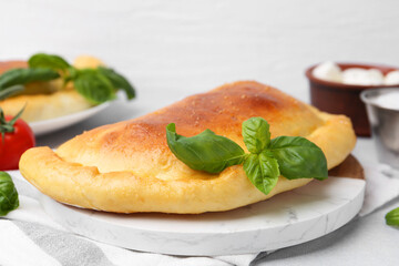 Tasty vegetarian calzone with basil on light table, closeup