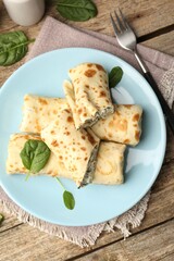 Tasty rolled crepes with cottage cheese and spinach served on wooden table, flat lay