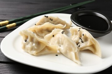 Delicious gyoza dumplings with sesame seeds served on black wooden table, closeup