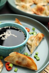 Fried gyoza dumplings with green onions, chili peppers and soy sauce on table, closeup