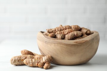 Raw turmeric roots in bowl on white table, closeup