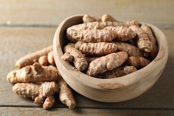 Raw turmeric roots in bowl on wooden table, closeup