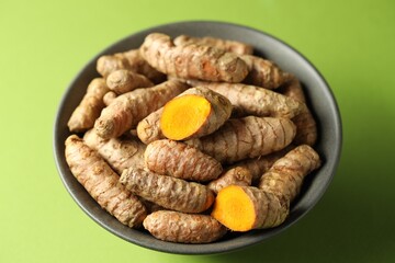 Tumeric rhizomes in bowl on green background, closeup