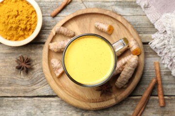 Delicious turmeric latte in glass cup, roots and spices on wooden table, flat lay